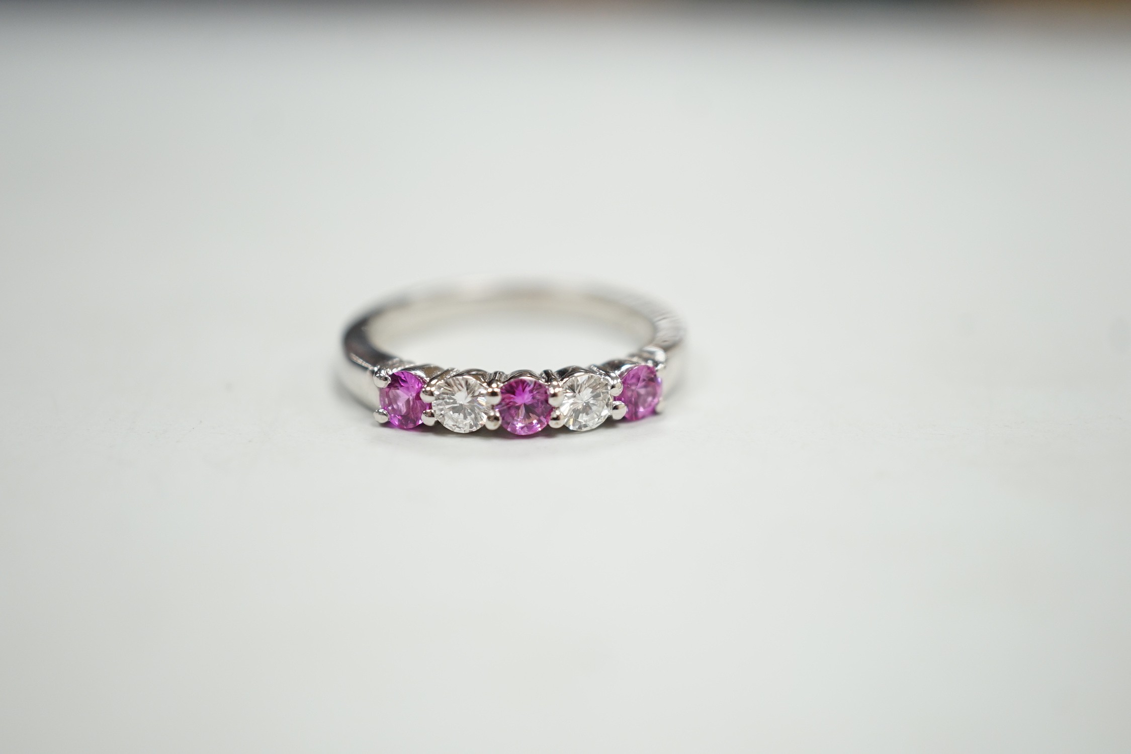 A modern 18ct white gold, three pink stone and two stone diamond set half hoop ring, size M, gross weight 4 grams.